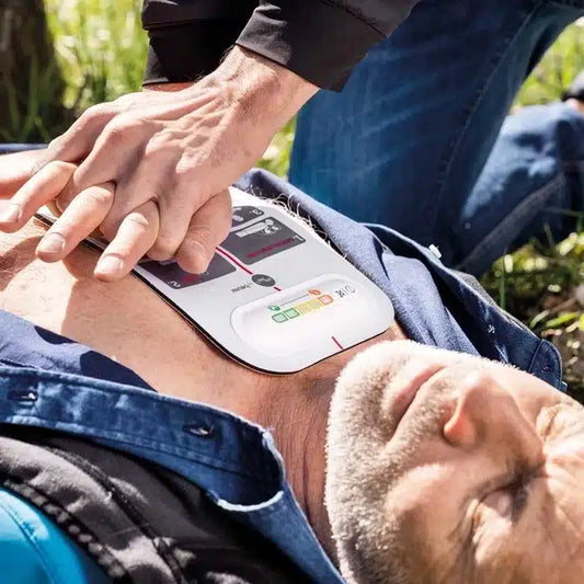 Ein erwachsener Mann erhält eine Herzdruckmassage mit dem innotas Beurer LifePad® Reanimationshilfe (Auslaufartikel, 1 Stück), während ein AED-Pad an seiner nackten Brust für eine effektive Erste Hilfe angebracht ist.