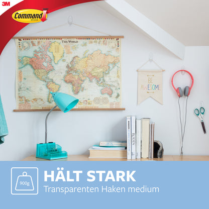 In einem hellen Raum hängen eine Weltkarte, ein "Be Awesome"-Schild und Kopfhörer an einem 3M Deutschland GmbH Command™ Haken M, mittelgroß, transparent (17091CLR), über einem Schreibtisch mit blauer Lampe und Büchern. Deutscher Text: "Hält stark. Rückstandsfrei. Transparenten Haken mittelgroß.