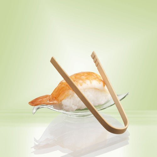 Ein Shrimp-Nigiri-Sushi wird auf einer Glasschale serviert, ergänzt durch PAPSTAR Fingerfood-Zangen aus Bambus (10 cm, 50 Stück) der PAPSTAR GmbH. Ein sanftes Hellgrün unterstreicht die umweltfreundliche Bambus-Präsentation.