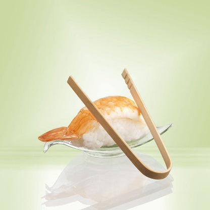Ein Shrimp-Nigiri-Sushi wird auf einer Glasschale serviert, ergänzt durch PAPSTAR Fingerfood-Zangen aus Bambus (10 cm, 50 Stück) der PAPSTAR GmbH. Ein sanftes Hellgrün unterstreicht die umweltfreundliche Bambus-Präsentation.