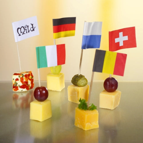 Six cheese cubes are topped with grapes or herbs and decorated for a stylish and eco-friendly presentation with the 8 cm large white deco-picker flags from PAPSTAR GmbH, with each flag labeled "Mild", Germany, Italy, Finland, Switzerland, or Belgium.