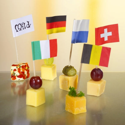 Six cheese cubes, each topped with a PAPSTAR 500 Deco-Picks 8 cm white from PAPSTAR GmbH. Some cubes are garnished with grapes, pickles, or herbs. The neutral, softly lit background ensures a stylish presentation.
