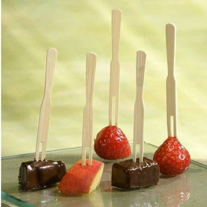 Auf fünf PAPSTAR Fingerfood-Spieße "pure" (8,5 cm) der PAPSTAR GmbH werden zwei Erdbeeren, zwei Schokowürfel und eine Apfelscheibe aufgespießt, die hochkant auf einem Glas vor hellgrünem Hintergrund präsentiert werden.