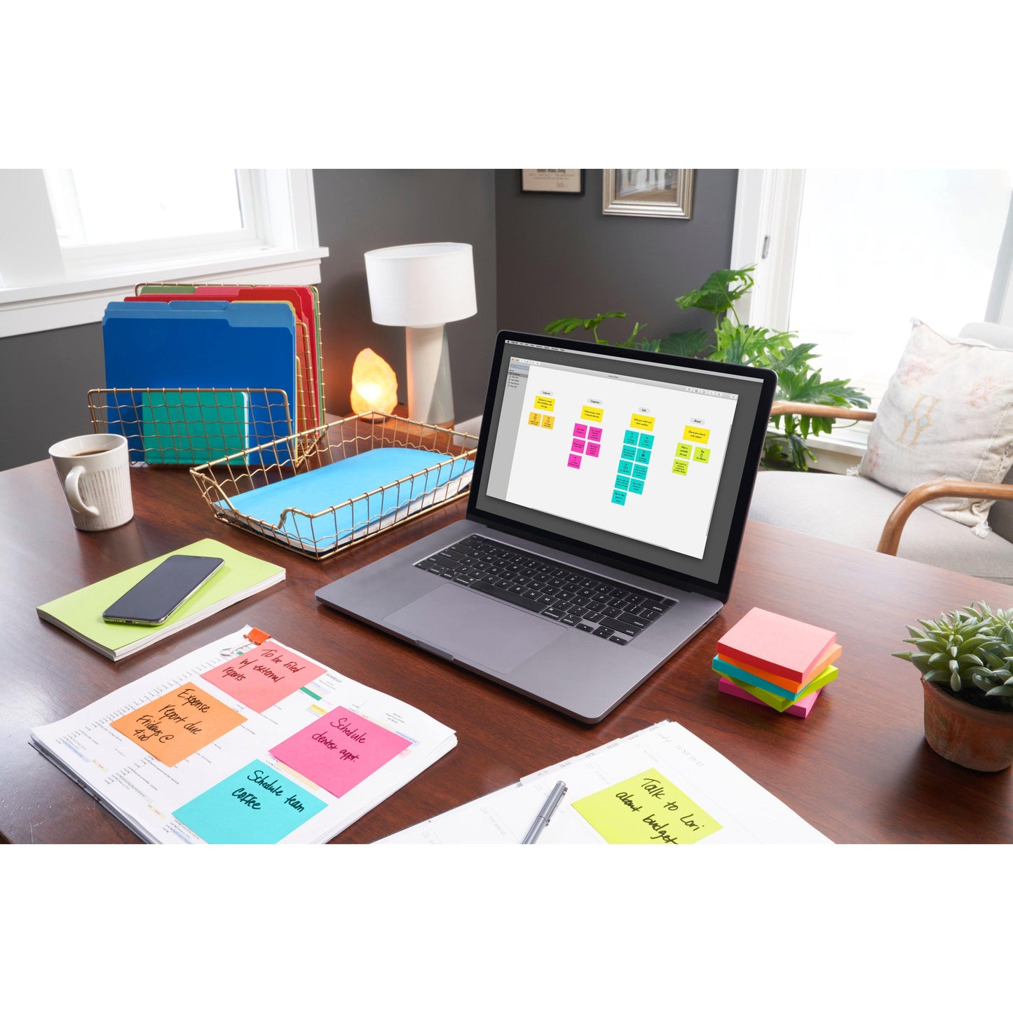 Ein Schreibtisch mit einem Laptop, auf dem ein Haftnotiz-Organizer, Post-it® Notes (76 mm x 76 mm, 100 Blatt/Block, 100% PEFC) von 3M Deutschland GmbH, Ordner, Papierkram, ein Telefon, eine Lampe, eine Pflanze und Sonnenlicht den organisierten Arbeitsbereich erhellen.