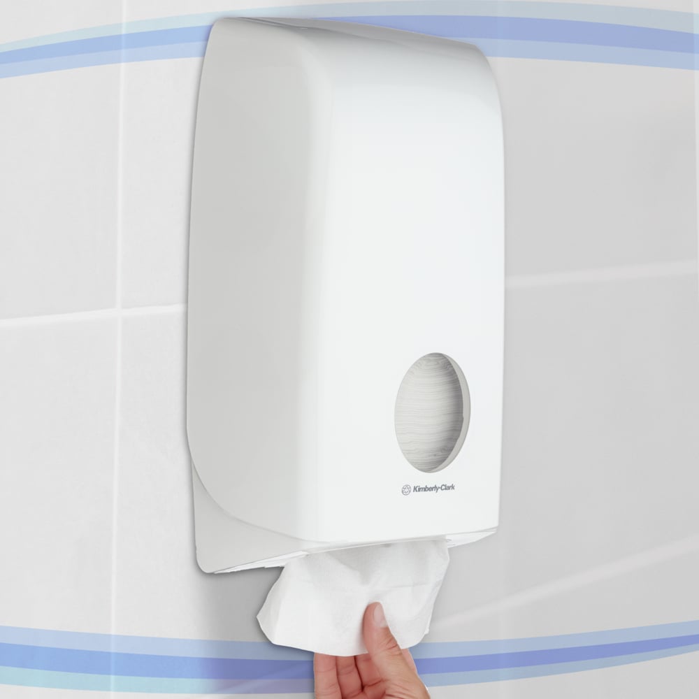 A hand pulls toilet paper from a white Aquarius™ toilet paper dispenser by Kimberly-Clark GmbH, which is wall-mounted for hygienic storage in a tiled bathroom.