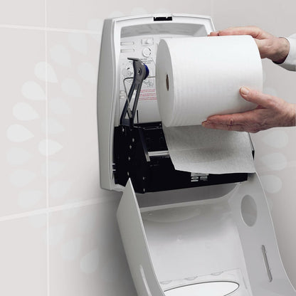 Eine Person lädt eine Kleenex® Ultra™ Handtücher - Rolle der Kimberly-Clark GmbH in einen weißen, offenen Wandspender in einer Toilette ein, um ein hygienisches Händetrocknen zu gewährleisten. Im Deckel des Spenders ist eine Anleitung aufgedruckt.