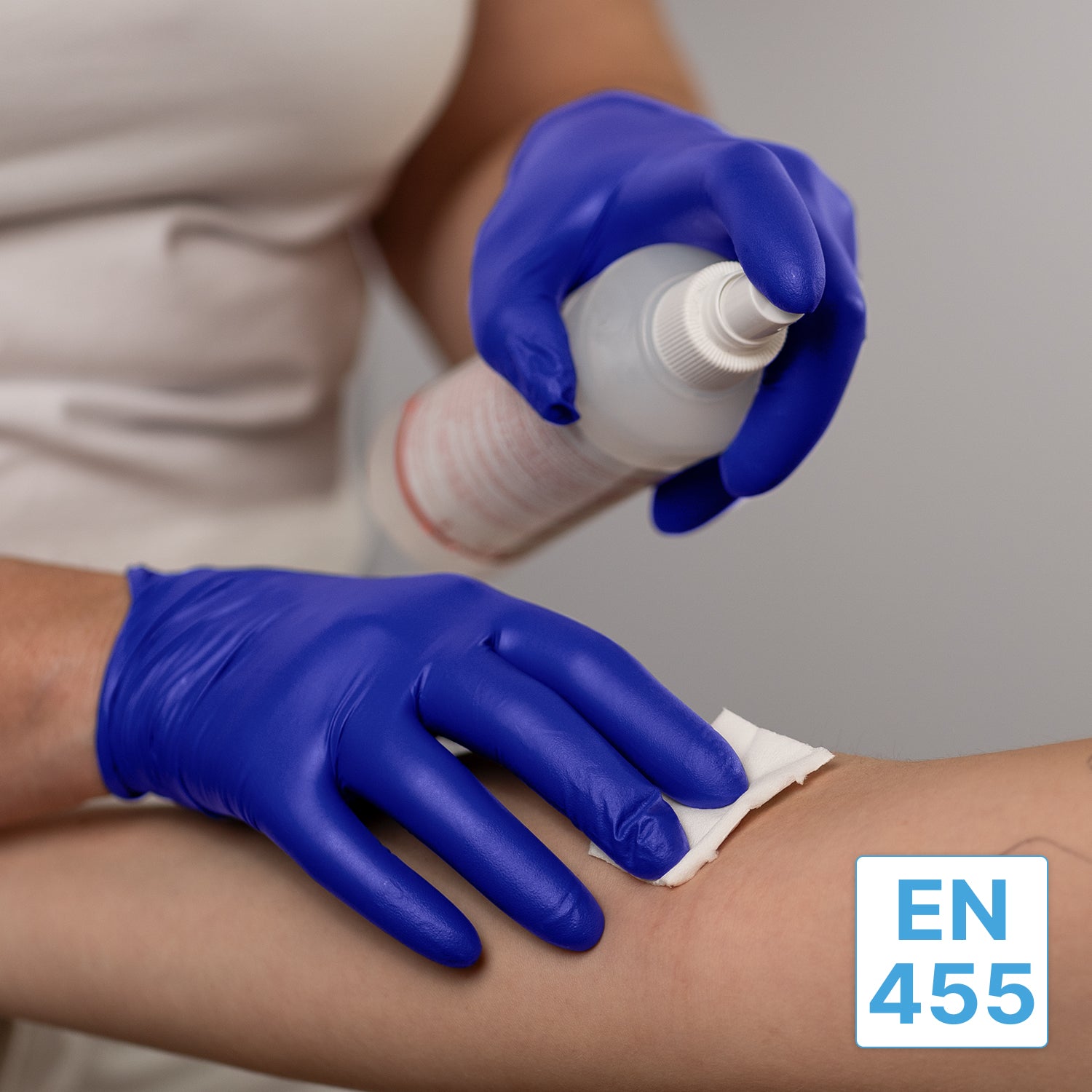 Eine Person, die ARNOMED NITRIL XTRA PURE Einmalhandschuhe aus Nitril von ARNOWA GmbH trägt, reinigt den Arm eines anderen mit einem weißen Tuch und einer Sprühflasche. Das Etikett "EN 455" erscheint in der rechten unteren Ecke des Bildes.