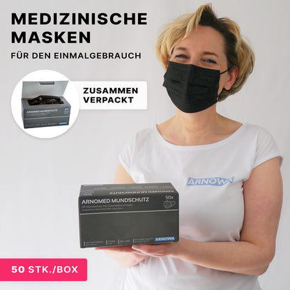 Eine Frau in schwarzem medizinischem Mundschutz und weißem Hemd hält eine Schachtel mit 50 ARNOMED MUNDSCHUTZ TYP IIR OP-Mundschutz mit Gummibändern von ARNOWA GmbH und weist darauf hin, dass diese Einwegmasken zusammen verpackt sind.