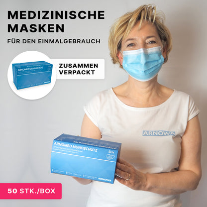 Eine Frau mit einer blauen medizinischen Maske hält eine Schachtel mit der Aufschrift "ARNOMED MUNDSCHUTZ TYP IIR OP-Mundschutz mit Gummibändern Typ IIR" der ARNOWA GmbH. Auf der Verpackung steht "Medizinische Masken für den Einmalgebrauch", 50 Stück pro Schachtel, mit einer Nahaufnahme abgebildet.