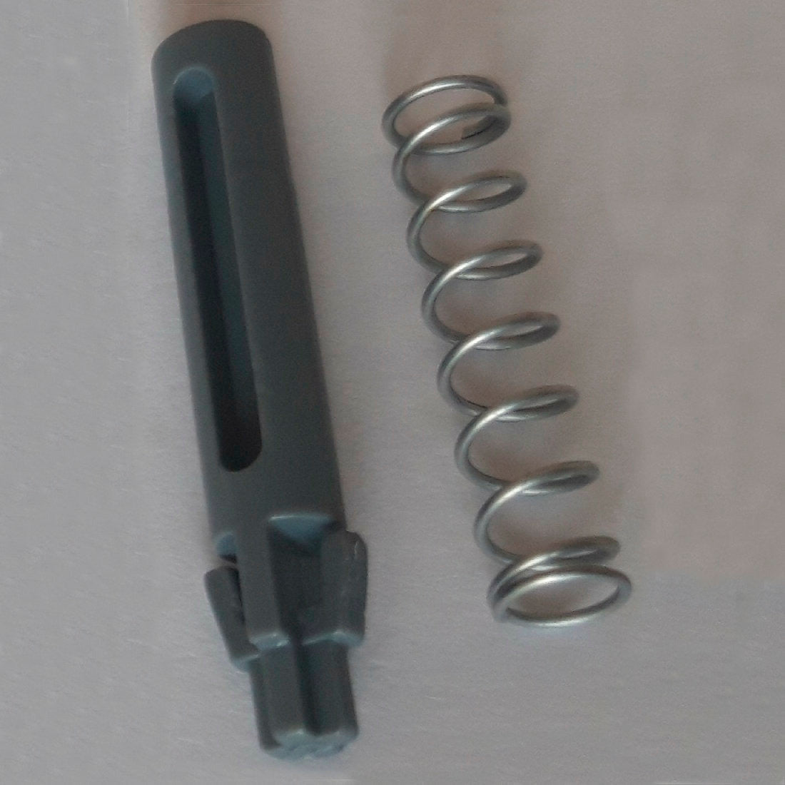 Un ressort métallique et un pivot de porte cylindrique gris foncé avec rainures et crans, faisant partie du pivot de porte & ressort DI Protect (1 pièce) de Diversey Deutschland GmbH & Co. OHG, sont illustrés sur une surface claire et montrent les matériaux robustes pour le chariot DI Protect.