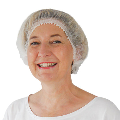 A smiling person wears the ARNOMED COVER PP-CLIP CAP XL disposable clip cap made of PP fleece (55cm) from ARNOWA GmbH and a white shirt, facing forward against a plain background, highlighting the excellent hygiene.