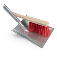 Set da pulizia Nölle Profi Brush (paletta in metallo zincato con scopa a mano da 28 cm, setole rosse) del marchio Nölle Profi Brush Bürsten- & Pinseltechnik e.K., con la scopa a mano posizionata in diagonale sulla paletta, su sfondo bianco.