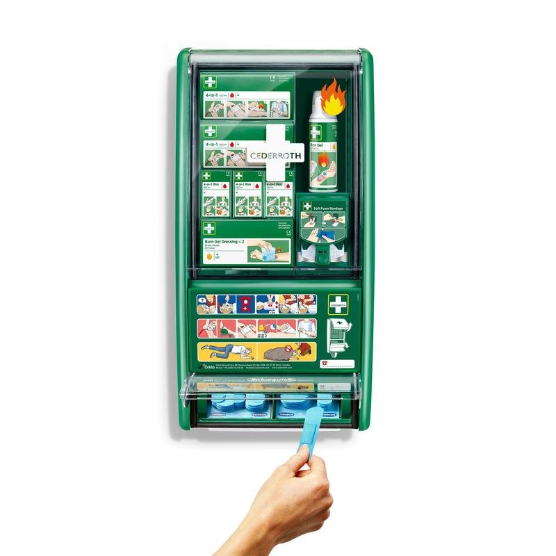 Una stazione di primo soccorso & ustioni Cederroth verde di Orkla Wound Care AB è montata su una parete bianca, fornita di bende, gel per ustioni, lavaggio oculare e altro. Una mano estrae una benda adesiva blu dal distributore inferiore della confezione da 1.