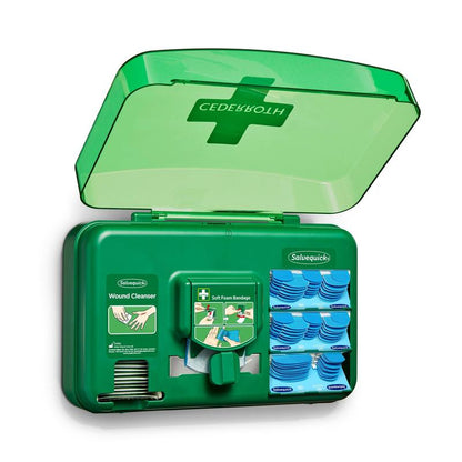 A blue wound care dispenser from Orkla Wound Care AB is open, revealing wound cleansing packets, plasters, and a roll of soft foam bandages arranged in individual compartments.