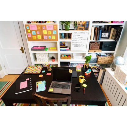 On the desk are a laptop, notebooks, a phone, pens, and a yellow mug. Post-it® Super Sticky Notes from 3M Deutschland GmbH (76 mm x 127 mm) are on the desk and the whiteboard next to books and baskets on the shelf.