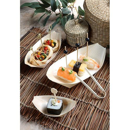 Finger food such as sushi and skewered wraps are served in PAPSTAR 50 finger food wooden bowls "pure" boats from PAPSTAR GmbH on a bamboo mat with baskets and green leaves in the background.