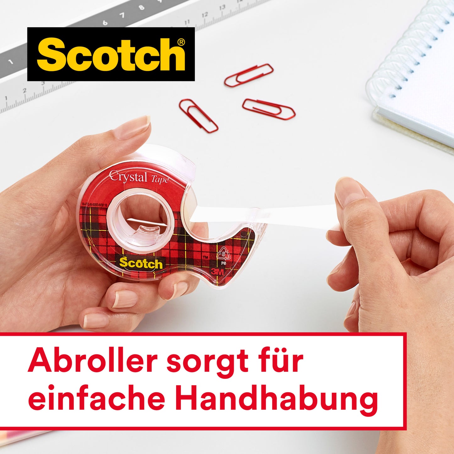Eine Person zieht Scotch® Crystal Klebeband, transparent, 19 mm x 33 m, von 3M Deutschland GmbH aus einem roten Tartan-Spender. In der Nähe: rote Büroklammern, Lineal, Spiralnotizbuch. Deutscher Text darunter: "Abroller sorgt für einfache Handhabung.
