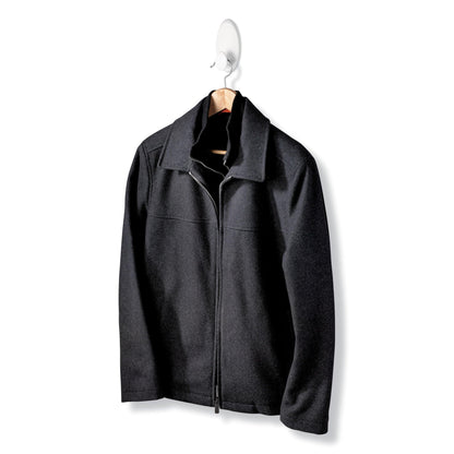 Eine schwarze Jacke mit Reißverschluss und Kragen hängt an einem Holzbügel des Command™ Kleider-Hakens, 17019-FGN, der eine Wandbefestigung ohne Bohren ermöglicht, vor einem schlichten weißen Hintergrund.