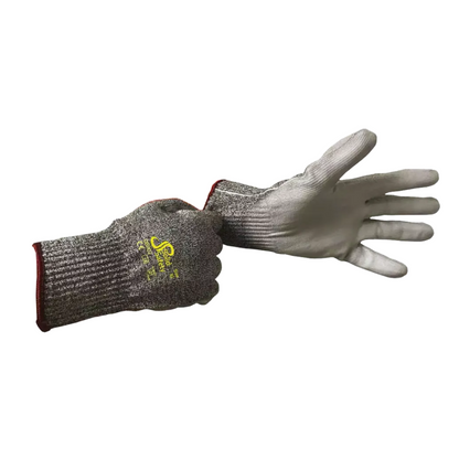 A person is wearing an AMPri SolidSafety Cut High cut-resistant glove made of cut-resistant materials on the left hand, while the right hand is holding the cuff of a second glove. These gray gloves from AMPri Handelsgesellschaft mbH are made of HPPE yarn with a yellow logo on the back, a ribbed texture, and a red cuff at the wrist.