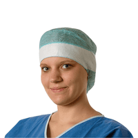 A young doctor is wearing a blue surgical gown and a Hartmann Foliodress® Cap Comfort Form Plus disposable surgical cap made of breathable viscose nonwoven fabric, and she is smiling gently at the camera. The background is plain white.