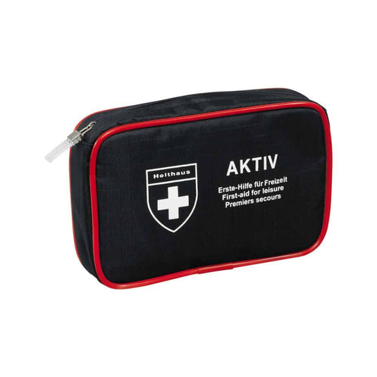 Un kit di pronto soccorso compatto, di colore nero, con rifiniture rosse e cerniera, un logo a forma di croce bianca e le scritte «Holthaus Medical AKTIV» e «Erste-Hilfe für Freizeit / First-aid for Leisure / Premiers secours» sul davanti. Perfetto sia in viaggio che a casa.