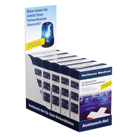 An exhibition booth displays several boxes of the Holthaus Medical Replacement Kit for Car First Aid Kits | Pack (1 piece) by Holthaus Medical GmbH & Co. KG. The sign at the top, featuring a blue siren image and German text, encourages customers to check their first aid supplies. The booth has a white base with blue accents and additional German text.