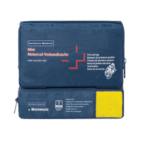 Une trousse de premiers secours bleue portant la mention « Holthaus Mini Combi Trousse de premiers secours pour moto » de la société Holthaus Medical GmbH & Co. KG, avec des instructions multilingues destinées aux motards. Elle est conforme à la norme DIN 13167 et contient un gilet de sécurité visible à travers une partie transparente. La trousse Mini Combi dispose de deux compartiments à fermeture éclair : l’un en haut et l’autre sur le côté.