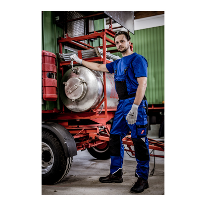 Dressed in a NITRAS MOTION TEX LIGHT T-shirt by AS Arbeitsschutz GmbH made of OEKO-TEX certified cotton for increased UV protection, a man stands next to a large metal tank on a red trailer. One hand rests on the tank, and in the background, a part of a green building or vehicle is visible.