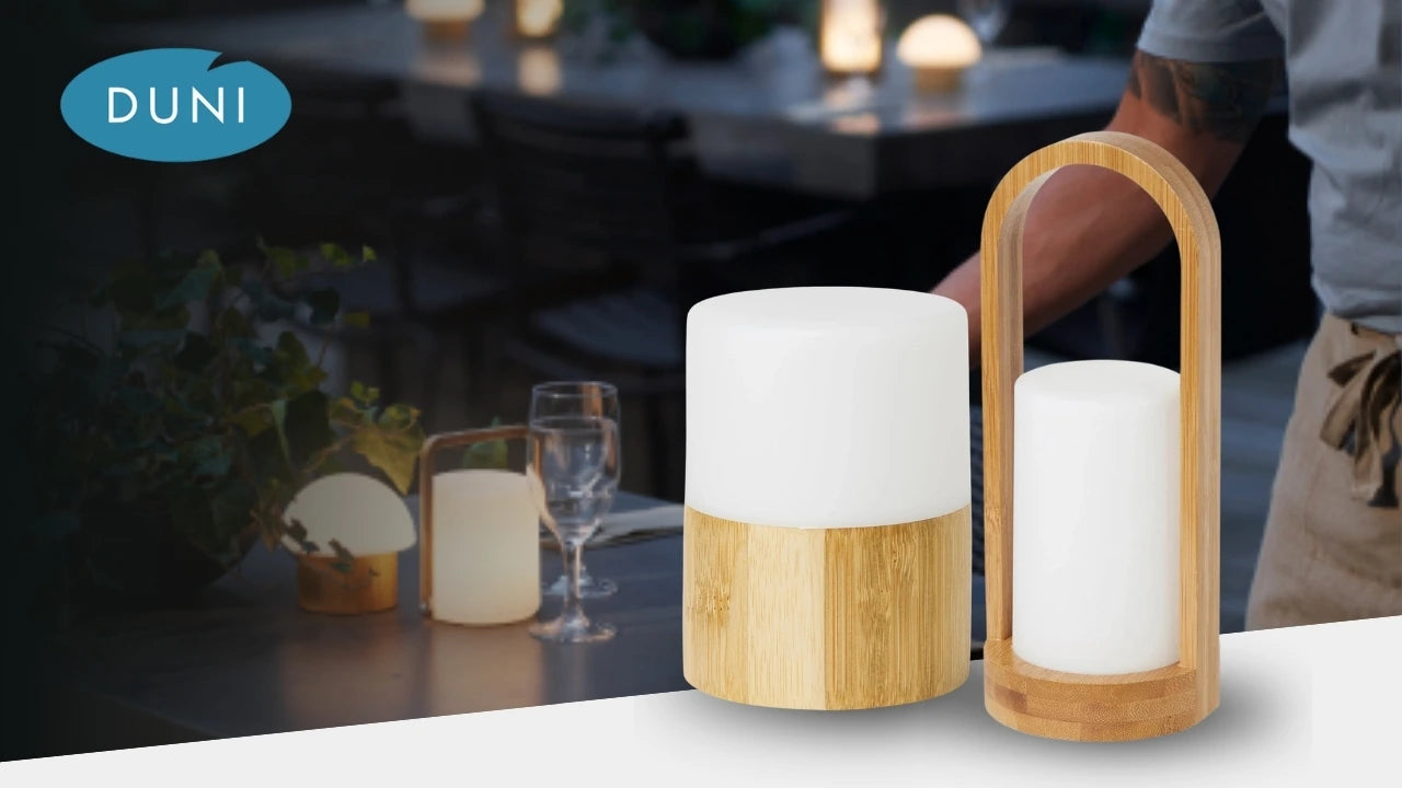 DUNI LED-Tischleuchten mit Holzsockel und warmweißem Licht, stilvoll inszeniert vor einer gemütlichen Restaurant-Atmosphäre mit gedecktem Tisch im Hintergrund.