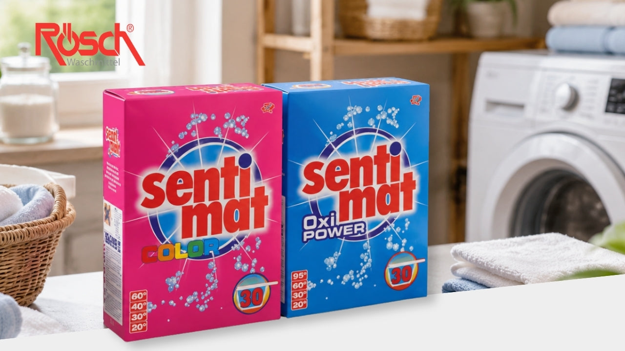 Zwei Packungen Senti Mat Waschmittel stehen auf einer Arbeitsfläche in einem hellen Waschraum: eine pinke Packung „Color“ und eine blaue Packung „Oxi Power“, jeweils für 30 Waschladungen. Im Hintergrund sind eine Waschmaschine, gefaltete Handtücher und ein Wäschekorb zu sehen. Oben links befindet sich das rote Rösch-Waschmittel-Logo.