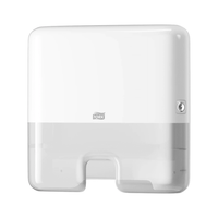 A Tork Xpress® 552100 Mini Dispenser for Elevation H2 Multifold Towels, manufactured by TORK – Essity Professional Hygiene Germany GmbH, is mounted on the wall. It features a simple rectangular design with rounded edges, a visible lock on the right side, and an opening at the bottom for dispensing Multifold towels one at a time.