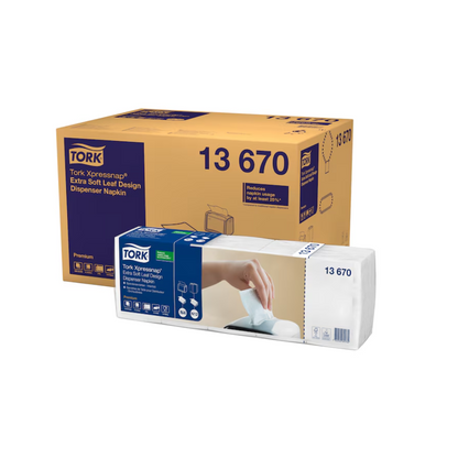 A Tork Xpressnap® 13670 dispenser napkin box with an extra soft leaf design from the brand TORK by Essity Professional Hygiene Germany GmbH is shown next to a package, where a hand pulls a napkin from the dispenser.