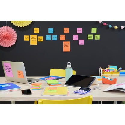 A desk with a laptop, tablet, calculator, phone, water bottle, and colorful stationery. Behind, Post-it® Super Sticky Notes (76x127mm) from 3M Deutschland GmbH arrange the school subjects on the wall, with decorations hanging above.