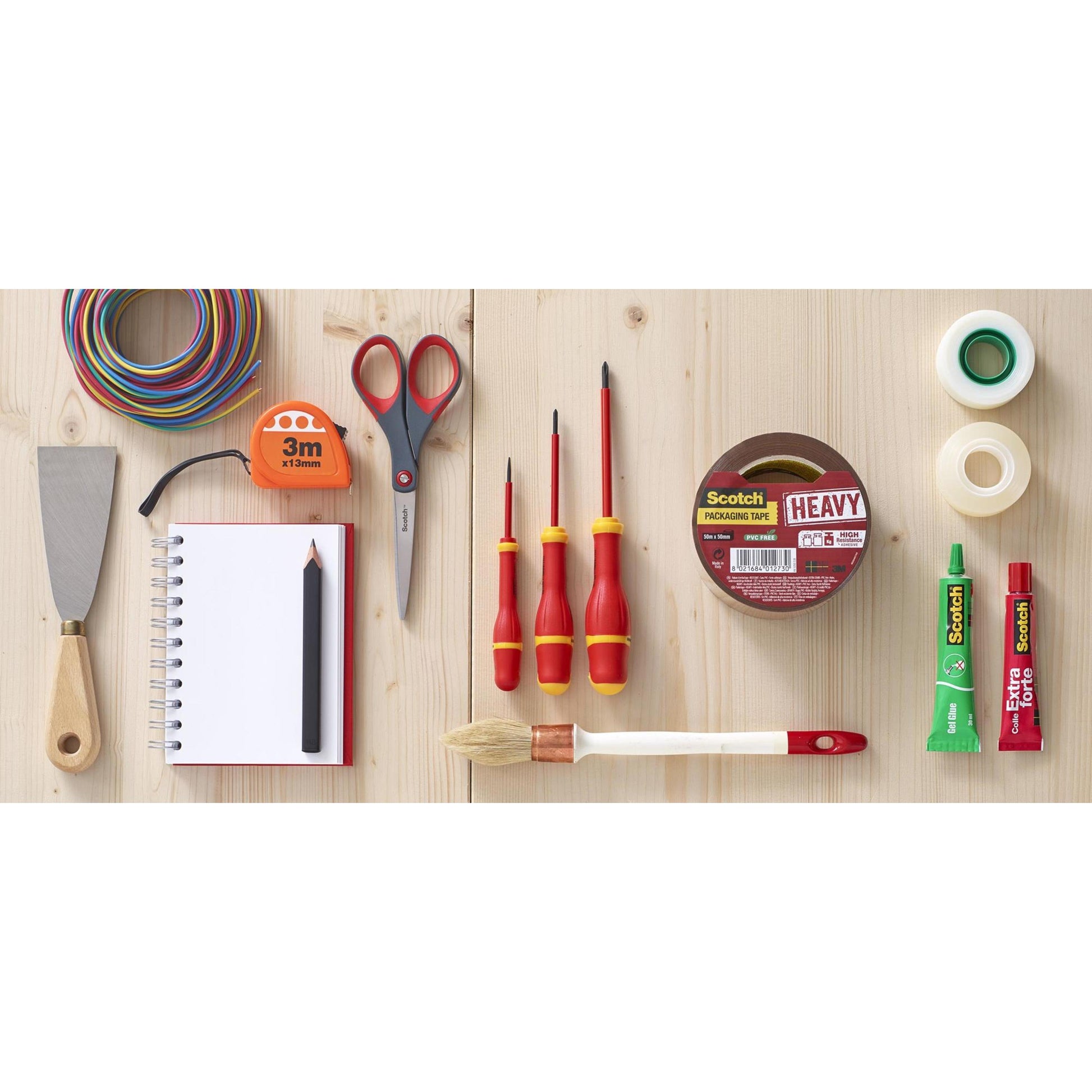 Eine Scotch™ Präzisionsschere rot der 3M Deutschland GmbH ist mit verschiedenen Werkzeugen und Schreibwaren wie farbigem Draht, Maßband, Schraubendreher, Klebeband, Spachtel, Spiralheft, Bleistift, Klebetube und Pinsel auf einer Holzfläche angeordnet.