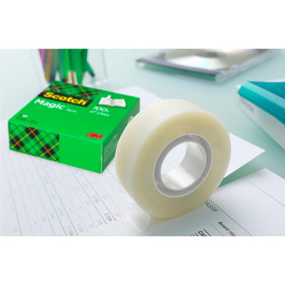 Eine Rolle 3M Deutschland GmbH Scotch® Magic™ Unsichtbares Klebeband (19 mm x 33 m) aus dem Vorteilspack mit 24 Rollen wird auf Papier abgerollt, während die grüne Schachtel mit der Aufschrift "Vorteilspack, 24 Stück" zwischen Büromaterialien steht.